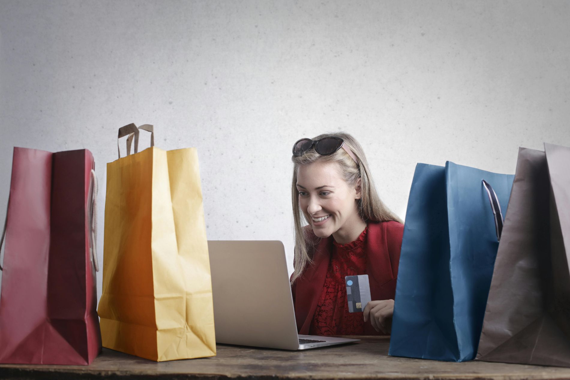 Blonde girl on a desk looking at laptop screen with 4 shopping bags around her